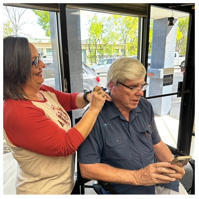 Woman examining man's ear with the EAR/BeBird X1 digital otoscope while he looks at his ear canal on his smartphone.